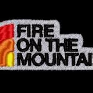 May include: Embroidered patch with the text "FIRE ON THE MOUNTAIN" in black, outlined in white. A stylized rainbow in red, orange, and yellow is on the left. The patch has a textured, stitched appearance and is set against a black background.