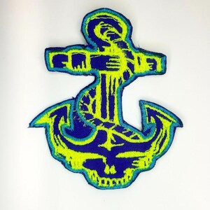 May include: Embroidered anchor patch in blue and neon yellow. The nautical design features a detailed anchor shape with a textured appearance. The patch is suitable for sewing onto clothing or accessories.