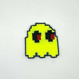 May include: A yellow pixelated ghost patch with black eyes and red pupils. The patch has a blue border and is reminiscent of a classic arcade game character. This embroidered patch is suitable for jackets, bags, or other fabric items.