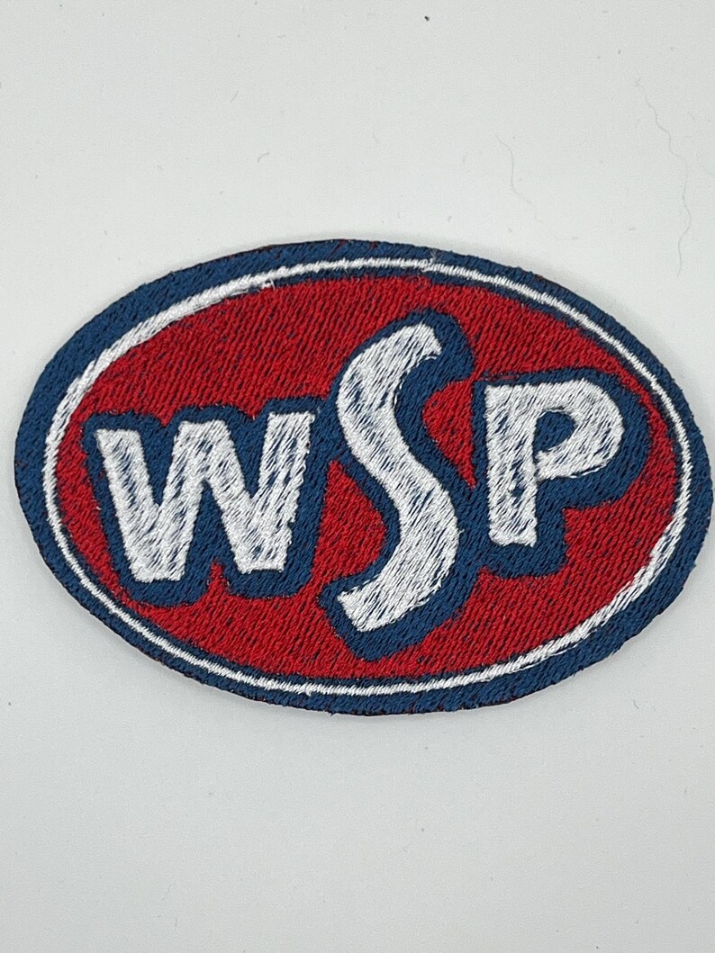 May include: Oval-shaped embroidered patch with the letters "WSP" in white, outlined in blue, set against a red background. The patch has a blue border and is likely designed for application on clothing or accessories.