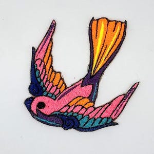 May include: Embroidered patch featuring a colorful swallow bird design. The bird has pink, orange, blue, and purple details. The patch is likely for clothing or accessories.