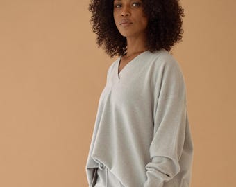 May include: A light gray v-neck sweater and matching sweatpants. The sweater has long sleeves and a relaxed fit.