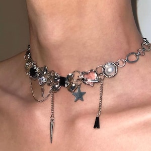 May include: Silver-toned choker necklace with various charms, including a star, heart, and a black bow. The necklace features dangling chains and a pearl accent, creating a unique and decorative accessory.