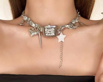 Op de afbeelding: Zilverkleurige choker-ketting met een vierkante horlogekast met Romeinse cijfers. De ketting bevat verschillende bedels: een hart, een ster en een punt. Het ontwerp bevat abstracte, organische vormen.
