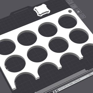 Puede incluir: Una bandeja rectangular blanca impresa en 3D con once recortes circulares y dos recortes semicirculares a lo largo de un borde. La bandeja tiene un peque&ntilde;o recorte cuadrado en la esquina superior derecha, sobre un fondo gris oscuro.