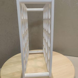 Puede incluir: Un botellero blanco de forma rectangular con numerosas aberturas ovaladas. El botellero est&aacute; hecho de madera y est&aacute; dise&ntilde;ado para guardar varias botellas. Se encuentra sobre una superficie de madera clara.