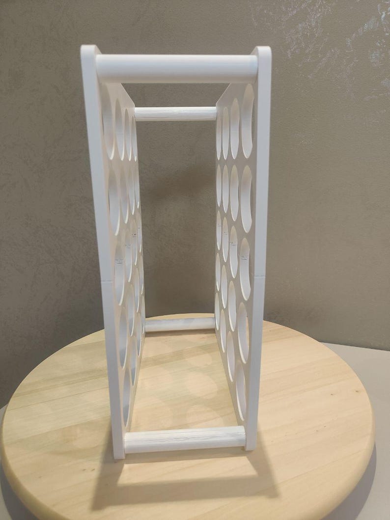 Puede incluir: Un botellero blanco de forma rectangular con numerosas aberturas ovaladas. El botellero est&aacute; hecho de madera y est&aacute; dise&ntilde;ado para guardar varias botellas. Se encuentra sobre una superficie de madera clara.