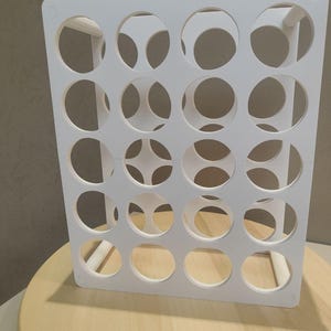 Puede incluir: Un organizador rectangular blanco con m&uacute;ltiples aberturas circulares. El organizador est&aacute; hecho de un material s&oacute;lido y est&aacute; dise&ntilde;ado para contener objetos. Se coloca sobre una superficie de madera de color claro.