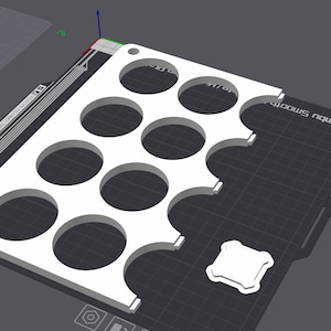 Puede incluir: Una bandeja rectangular blanca impresa en 3D con m&uacute;ltiples recortes circulares. La bandeja tiene un patr&oacute;n de rejilla y una peque&ntilde;a pieza cuadrada al lado. El fondo es una superficie gris oscuro.