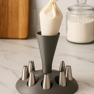 May include: A grey icing bag holder with a white piping bag filled with cream. The holder has a circular base with several stainless steel decorating nozzles. A wooden chopping board and a jar of flour are in the background.