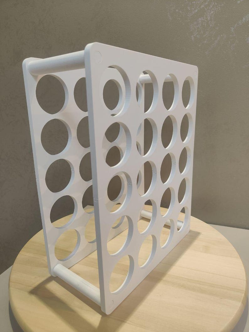 Puede incluir: Un organizador blanco de marco abierto con m&uacute;ltiples aberturas circulares. La estructura es rectangular con una barra en forma de asa en la base. El organizador est&aacute; dise&ntilde;ado para contener m&uacute;ltiples art&iacute;culos. El art&iacute;culo est&aacute; sobre una superficie de madera.