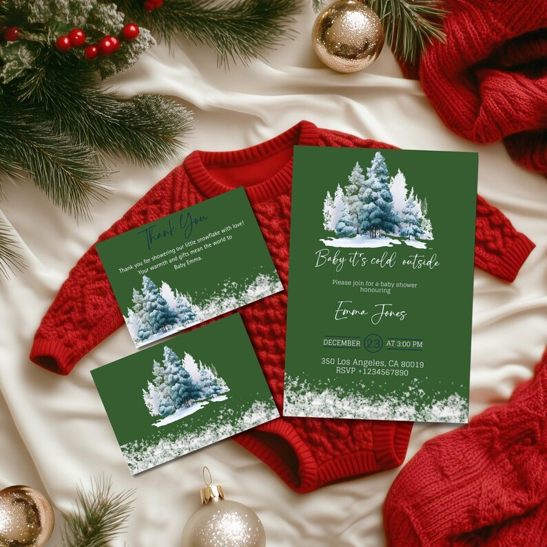 May include: A festive baby shower invitation set with a forest design. The set includes a large invitation and two smaller thank you cards. The invitations are green with a winter forest scene and the text "Baby it's cold outside". A red baby onesie is in the background.