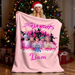 May include: A white ceramic mug with a black handle and the text "But First, Coffee" in a bold, black font. The mug is set against a blurred background, suggesting a cozy setting.