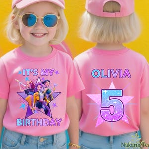 May include: Pink t-shirts with a birthday theme. The front of the shirt says "IT'S MY BIRTHDAY" with a star graphic and cartoon characters. The back of the shirt says "OLIVIA" and the number "5" in a star graphic.