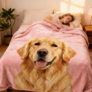 May include: A pink fleece blanket featuring a large, smiling Golden Retriever dog face. The blanket has the name "Sophia" in white script. The blanket is on a bed with a person sleeping under it.