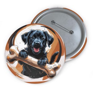 May include: A round button featuring a black Labrador puppy holding a bone. The puppy is smiling with its tongue out, set against a brown and white background. A second button with a pin back is visible.