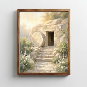 Puede incluir: Una pintura enmarcada representa una tumba abierta tallada en un acantilado de piedra. Una gran piedra redonda descansa junto a la entrada. Unas escaleras conducen a la tumba, y la escena está bañada en una luz suave. El follaje verde y las flores blancas enmarcan el camino.