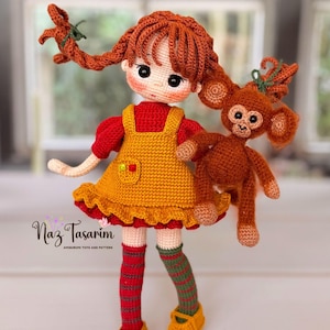 May include: A crocheted doll with auburn hair in pigtails, wearing a red shirt and yellow pinafore dress, holding a small brown crocheted monkey. The doll has striped socks and yellow shoes. Text on the image reads Naz Tasarim AMIGURUMI TOYS AND PATTERN.