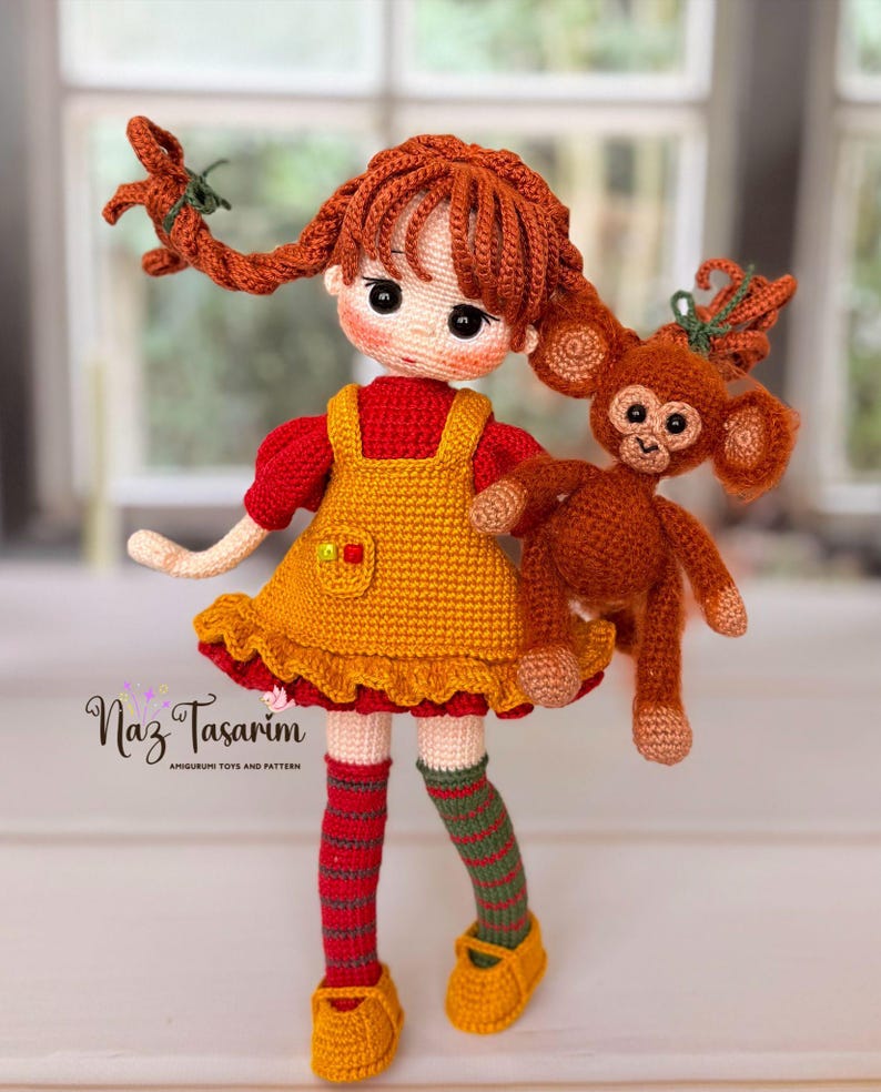 May include: A crocheted doll with auburn hair in pigtails, wearing a red shirt and yellow pinafore dress, holding a small brown crocheted monkey. The doll has striped socks and yellow shoes. Text on the image reads Naz Tasarim AMIGURUMI TOYS AND PATTERN.