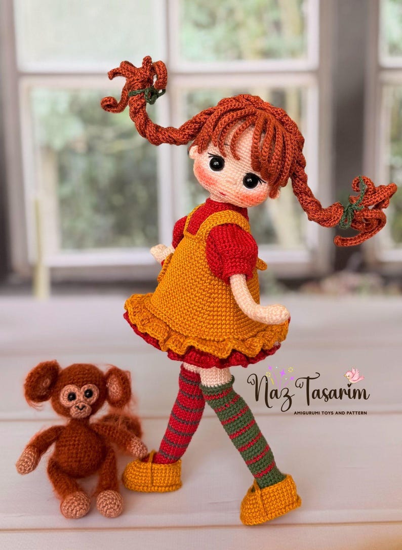 May include: A crocheted doll with red braided hair, wearing a yellow dress over a red shirt, and striped green and red stockings with yellow shoes, accompanied by a small brown crocheted monkey. The text Naz Tasarım is visible.