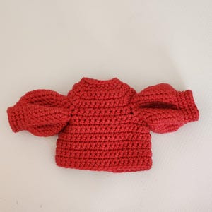 May include: A vibrant red crochet top featuring a high neckline and voluminous puff sleeves. The garment is constructed with a dense, textured stitch pattern throughout, showcasing a structured bodice and gathered sleeve cuffs in a solid red yarn.