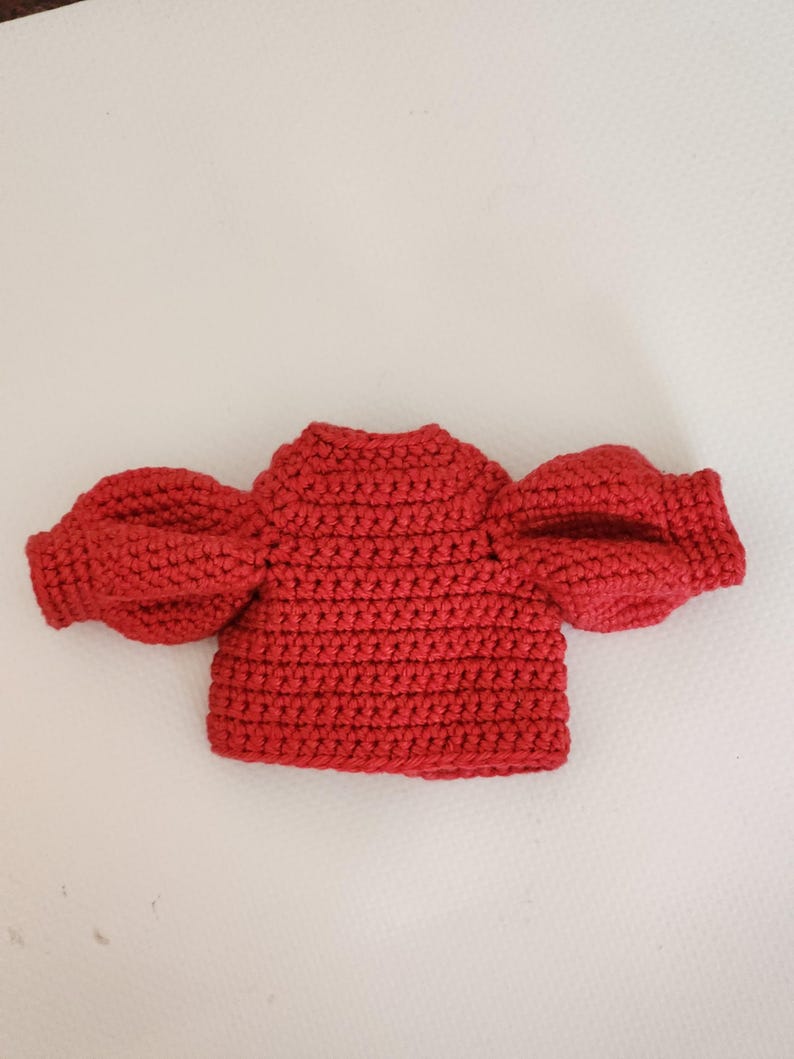 May include: A vibrant red crochet top featuring a high neckline and voluminous puff sleeves. The garment is constructed with a dense, textured stitch pattern throughout, showcasing a structured bodice and gathered sleeve cuffs in a solid red yarn.