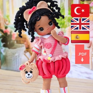 May include: A handmade crochet doll with black curly hair, wearing a pink dress and shorts. The doll has a teddy bear purse and is adorned with a bow. The doll's outfit includes white and rainbow striped leg warmers.