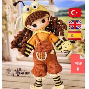 May include: A handcrafted crochet doll in a bee costume. It has a yellow hat with antennae and wings, brown curly hair, and an orange jumpsuit with black and yellow striped sleeves and socks. The doll holds a bee-shaped plush toy.