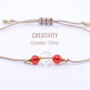 Puede incluir: Una pulsera beige ajustable con cuentas de cornalina roja y citrino transparente, con detalles dorados. El texto "CREATIVITY" y "Carnelian • Citrine" se muestra en la imagen.
