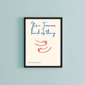 May include: A black framed print with a white background. The print features blue text that reads "It's a Forever kind of thing" and a red line drawing of two arms hugging.