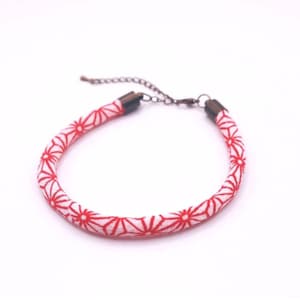 Op de afbeelding: Een rood-wit patroonarmband met een bloemmotief. De armband heeft een witte achtergrond met rode bloempatronen. De armband heeft een bronskleurige ketting en eindkappen. De armband is ongeveer 18 cm lang.