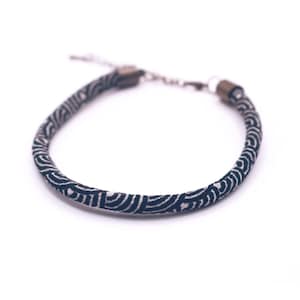 Op de afbeelding: Een marineblauw en wit patroonarmband met een zilverkleurige ketting en sluiting. De armband heeft een herhalend golfachtig ontwerp. De armband wordt getoond op een witte achtergrond.