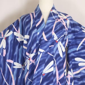 Puede incluir: Un kimono azul oscuro con un patrón repetitivo de libélulas blancas con detalles rojos y líneas de color rosa claro que imitan pinceladas. La prenda tiene mangas anchas, un cuello en V y un acabado suave y satinado en toda la tela.