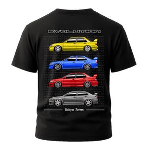 Puede incluir: Camiseta negra con ilustraciones de coches Mitsubishi Lancer Evolution amarillos, azules, rojos y grises. La palabra "EVOLUTION" está impresa en la parte superior y "Tokyo Toms" en la inferior.