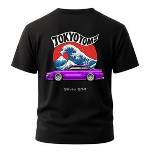 May include: Black t-shirt featuring a graphic of a purple car with the text "Silvia S14" below it. Above the car is a design of a red sun, a blue wave, and a mountain, with the text "TOKYO TOMS" in white.
