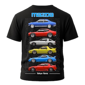 May include: Black t-shirt featuring a graphic of several Mazda RX-7 and RX-8 cars in various colors. The Mazda logo is at the top, and the text "Tokyo Toms" is at the bottom. The cars are blue, red, silver, yellow, and blue.