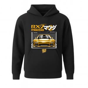 Könnte beinhalten: Schwarzer Kapuzenpullover mit einer goldenen Illustration eines Mazda RX-7-Autos in einer Garage. Das Design enthält japanischen Text und die Worte "Tokyo Toms".