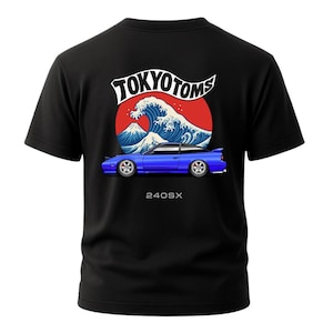 May include: Black t-shirt featuring a blue sports car design with the text "240SX" below it. The graphic includes a red circle, a white wave, and the text "TOKYO TOMS" in a stylized font. The shirt is short-sleeved.