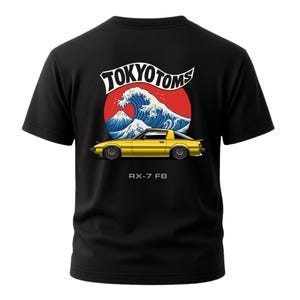 May include: Black t-shirt featuring a yellow sports car design with the text "TOKYO TOMS" above a wave and mountain graphic. The text "RX-7 FB" is below the car.