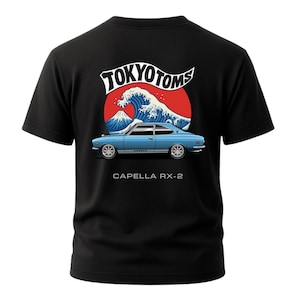 May include: Black t-shirt featuring a blue Capella RX-2 car graphic. The design includes the text "TOKYO TOMS" above a wave and mountain scene. The text "CAPELLA RX-2" is below the car.