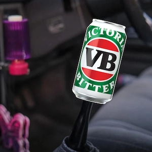 May include: A silver can of Victoria Bitter beer with a red and green label. The can is attached to a black gear stick. The text "VICTORIA BITTER" is visible on the can.