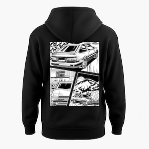 May include: Black hoodie featuring a black and white graphic of a car in a comic book style. The graphic shows the car in three different scenes, with a mountain and building in the background.