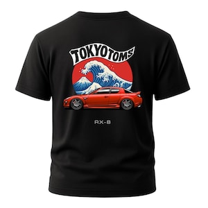 May include: Black t-shirt featuring a graphic design with the text "TOKYO TOMS" above a red sports car, a blue wave, and a red circle. The text "RX-8" is below the car. The design is inspired by Japanese art.