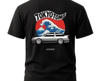 May include: Black t-shirt featuring a graphic of a white car with the text "AE86" below it. The design includes a red circle with a blue wave and mountain scene, and the words "TOKYO TOMS" in white.