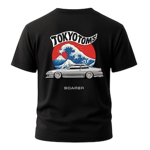 May include: Black t-shirt featuring a graphic design with the text "TOKYO TOMS" above a wave and a car illustration. The design includes a red circle and the word "SOARER" below the car.