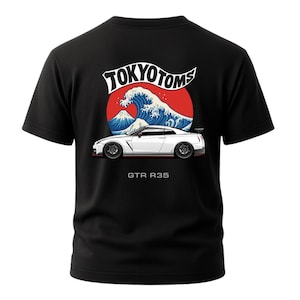 May include: Black t-shirt featuring a white sports car graphic with the text "GTR R35" below it. Above the car is a design with the text "TOKYO TOMS", a red circle, a blue wave, and a mountain.