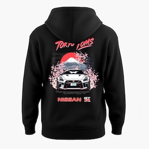 Könnte beinhalten: Schwarzer Kapuzenpullover mit einer Grafik eines weißen Sportwagens vor dem Berg Fuji, mit Kirschblüten und einer roten Sonne. Der Text "Tokyo Toms" und "Nissan" sind in Rot und Weiß.