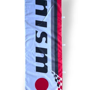 Könnte beinhalten: Weißes Banner mit dem Wort "nism" in großen schwarzen Buchstaben. Das Banner hat einen roten Kreis am unteren Rand und ein Design aus roten, grauen und schwarzen Streifen auf der rechten Seite. Ein Schachbrettmuster befindet sich unten rechts.