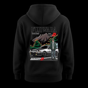 Könnte beinhalten: Schwarzer Kapuzenpullover mit einer Grafik eines weiß-schwarzen Autos, einer Person und dem Text "FUJIWARA TAKUMI" und "PROJECT-D". Das Design beinhaltet eine Berglandschaft und japanischen Text.