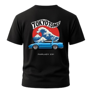May include: Black t-shirt featuring a blue Fairlady Z31 car graphic with a Japanese wave and mountain design. The text "TOKYO TOMS" is arched above the graphic, with "FAIRLADY Z31" below. The design is in shades of blue, red, and white.